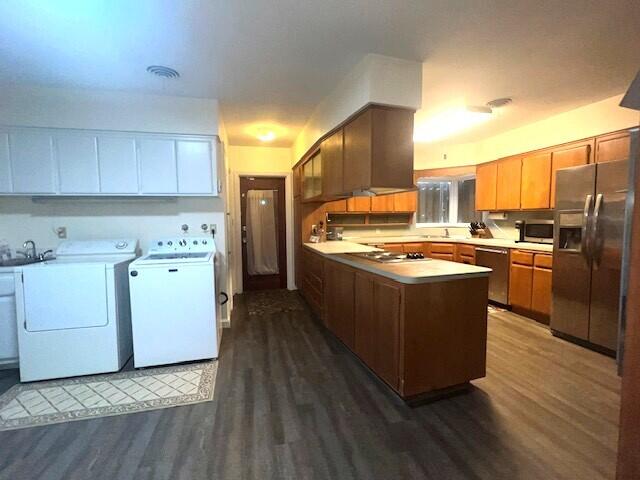 kitchen with appliances with stainless steel finishes, dark hardwood / wood-style floors, sink, kitchen peninsula, and washer and clothes dryer