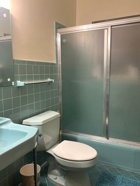 bathroom featuring enclosed tub / shower combo, tile patterned floors, toilet, and tile walls