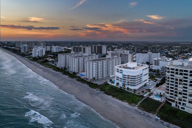 aerial view at dusk featuring a view of the beach, a water view, and a view of city