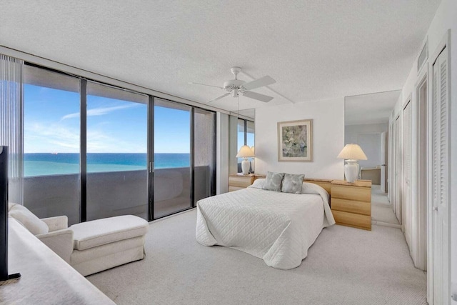 bedroom with ceiling fan, a water view, a textured ceiling, light carpet, and access to outside