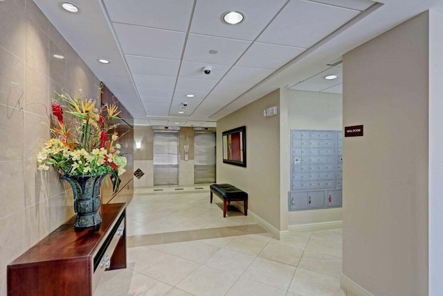 corridor featuring a drop ceiling, tile walls, mail boxes, and light tile patterned floors