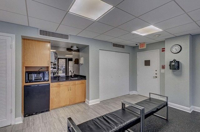 interior space with black microwave, sink, a drop ceiling, and light wood-type flooring