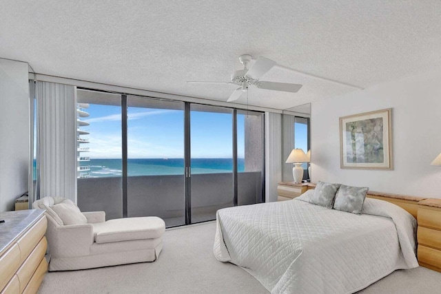 carpeted bedroom with a water view, ceiling fan, a view of the beach, and a textured ceiling