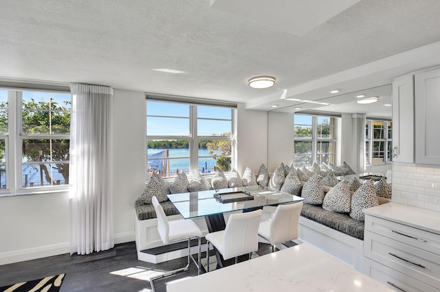 dining area featuring dark wood-type flooring, a textured ceiling, and a water view