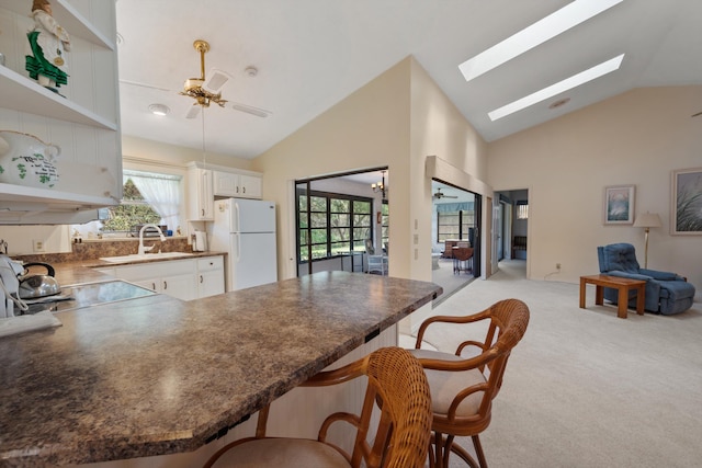 kitchen with freestanding refrigerator, white cabinetry, open shelves, a kitchen bar, and dark countertops