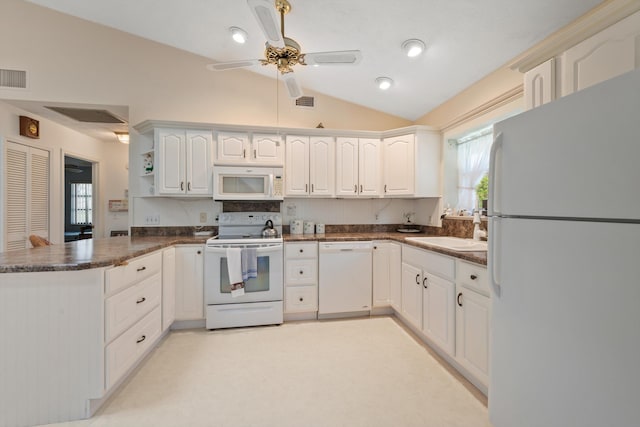 kitchen featuring dark countertops, a sink, white cabinets, a peninsula, and white appliances