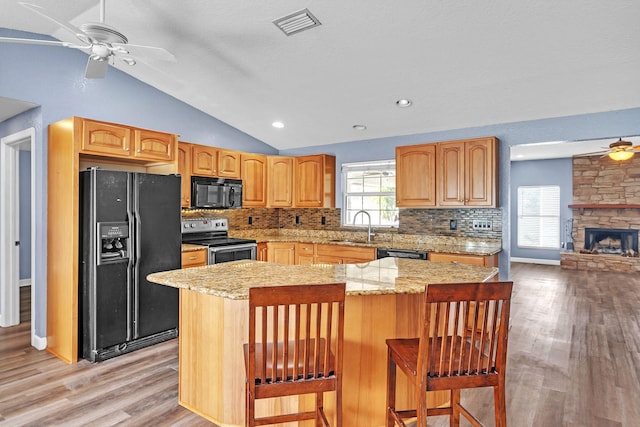 kitchen with a center island, a breakfast bar, lofted ceiling, and black appliances