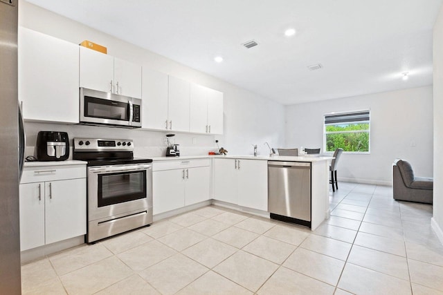 kitchen with sink, white cabinetry, light tile patterned floors, appliances with stainless steel finishes, and kitchen peninsula