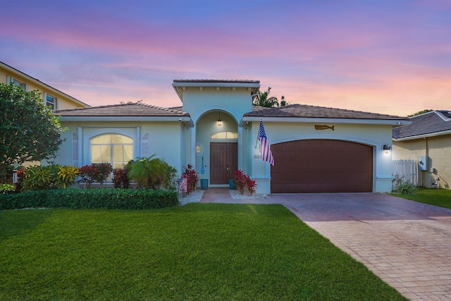 view of front of home with an attached garage, a tile roof, decorative driveway, a lawn, and stucco siding