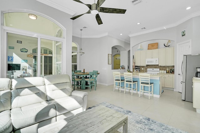 living room with arched walkways, light tile patterned floors, a ceiling fan, baseboards, and ornamental molding