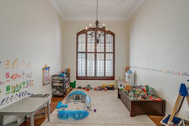 playroom with ornamental molding, a notable chandelier, and wood finished floors