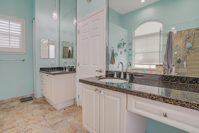 bathroom with two vanities, a sink, a tile shower, and baseboards