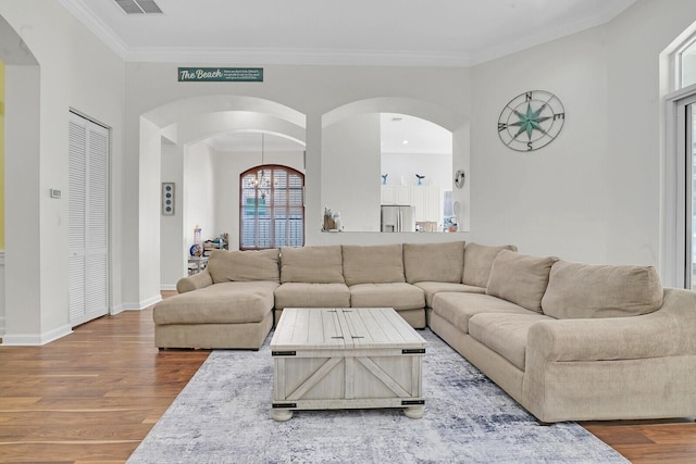 living room featuring baseboards, visible vents, arched walkways, wood finished floors, and crown molding