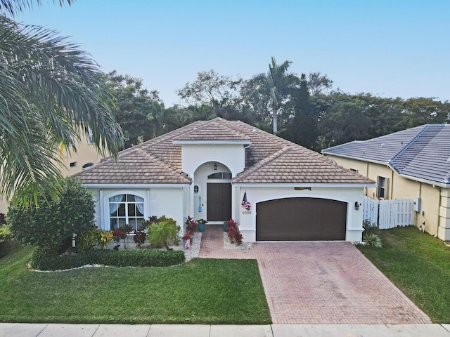 mediterranean / spanish house featuring an attached garage, fence, decorative driveway, stucco siding, and a front yard