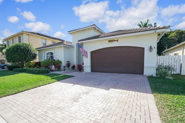 view of front facade with decorative driveway, stucco siding, a front yard, fence, and a garage