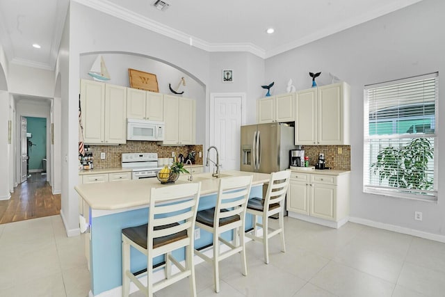 kitchen with white appliances, crown molding, a breakfast bar, a kitchen island with sink, and tasteful backsplash