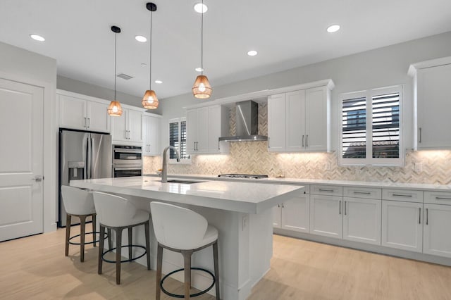 kitchen with a kitchen breakfast bar, light countertops, stainless steel appliances, wall chimney range hood, and a sink