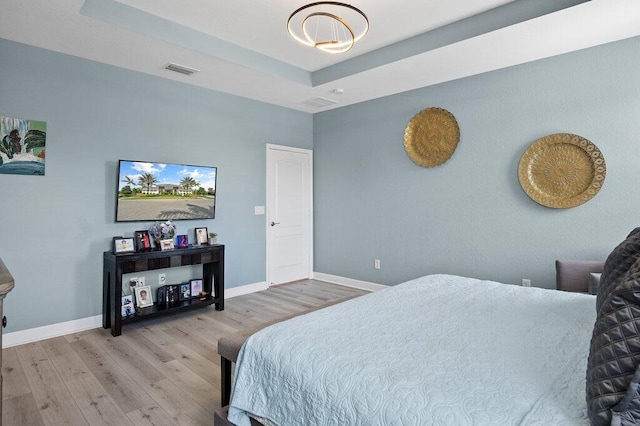 bedroom with a tray ceiling and light wood-type flooring