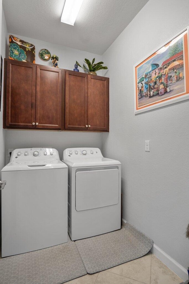 washroom with cabinets, washing machine and dryer, light tile patterned floors, and a textured ceiling