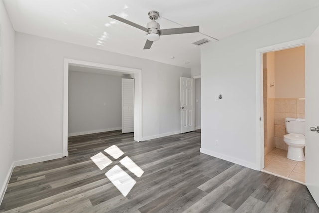 unfurnished bedroom with ceiling fan, dark hardwood / wood-style floors, ensuite bath, and tile walls