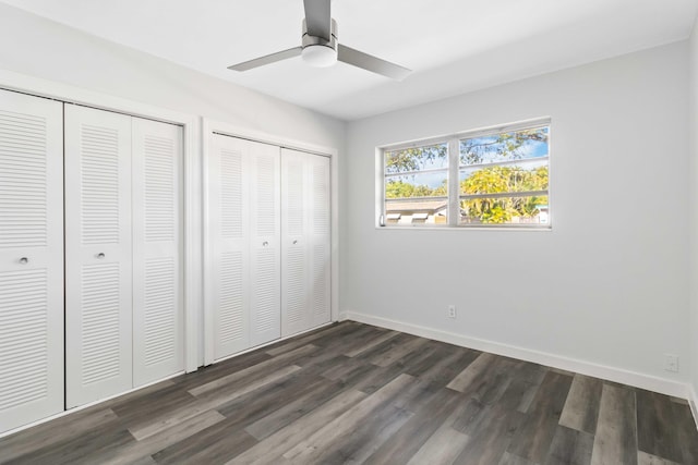 unfurnished bedroom with dark hardwood / wood-style flooring, two closets, and ceiling fan