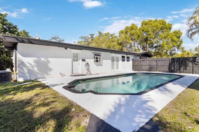 rear view of property with central AC unit, a fenced in pool, a patio, and a lawn