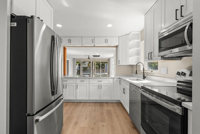 kitchen with stainless steel appliances, white cabinetry, sink, and light hardwood / wood-style flooring