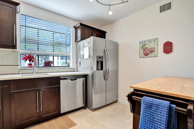 kitchen with sink, light tile patterned flooring, stainless steel appliances, dark brown cabinets, and tasteful backsplash