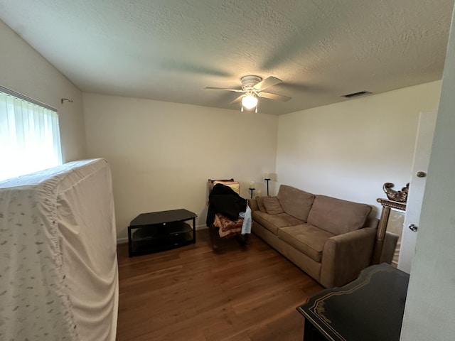 living room featuring ceiling fan, dark wood-type flooring, and a textured ceiling