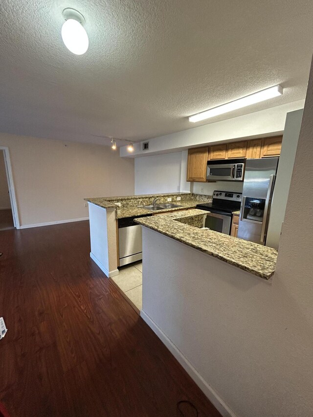 kitchen with a peninsula, appliances with stainless steel finishes, a sink, light wood-type flooring, and a textured ceiling