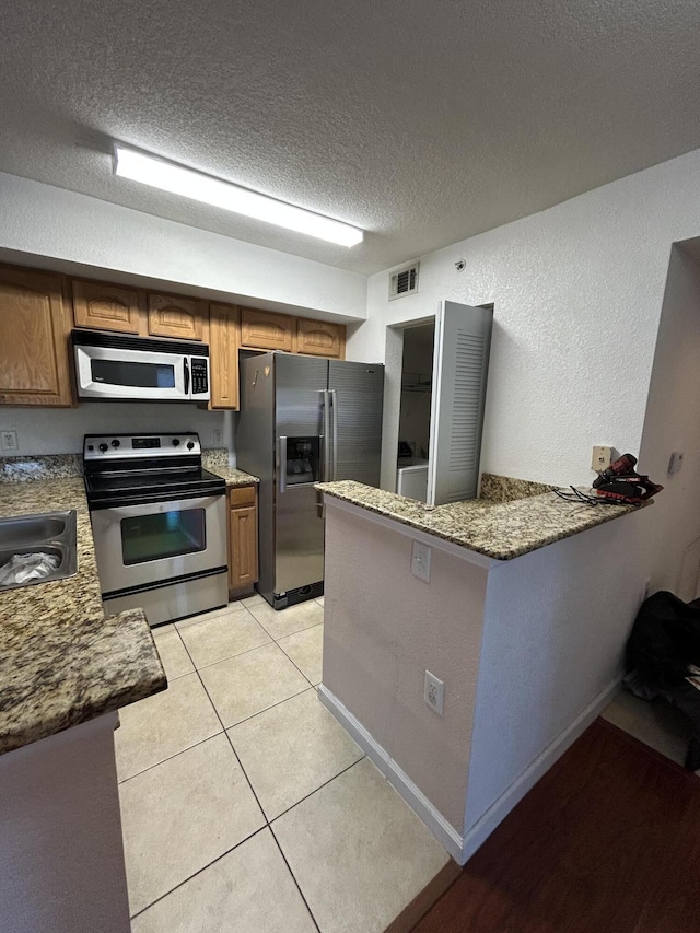 kitchen featuring appliances with stainless steel finishes, a textured ceiling, visible vents, and brown cabinetry