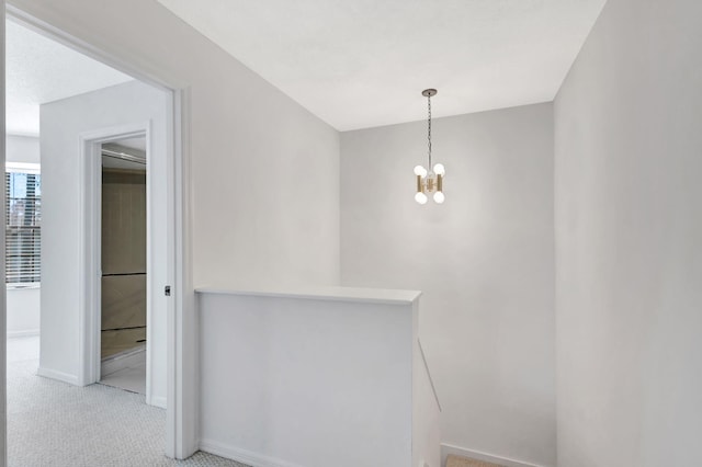 hall featuring light carpet and a notable chandelier