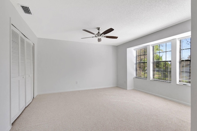 unfurnished bedroom featuring ceiling fan, light carpet, a textured ceiling, and a closet