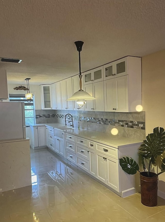 kitchen with sink, white cabinets, backsplash, and decorative light fixtures