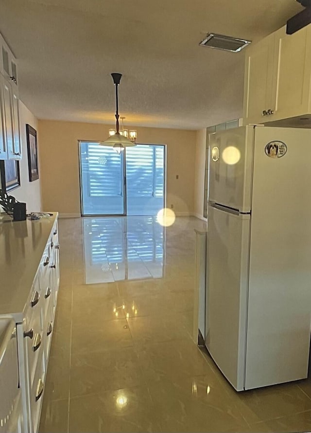 kitchen with white refrigerator, sink, hanging light fixtures, and white cabinets