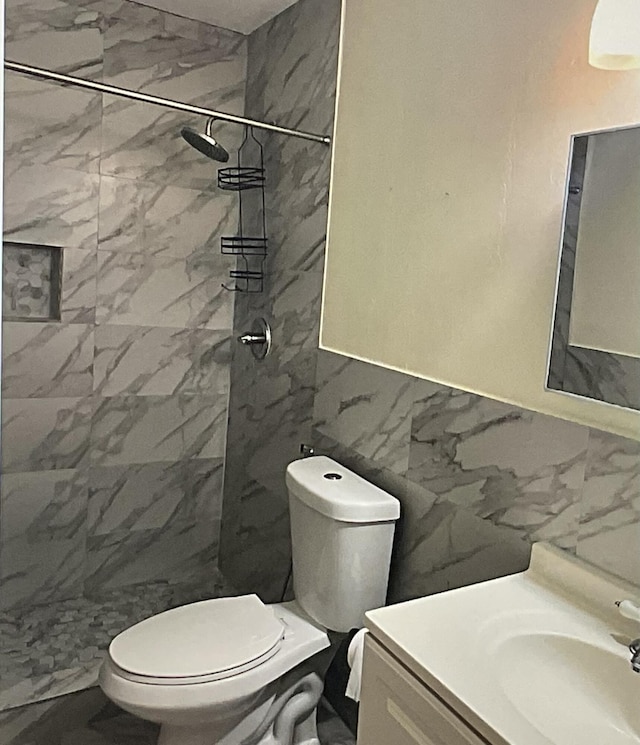 bathroom with vanity, tile walls, toilet, and tiled shower