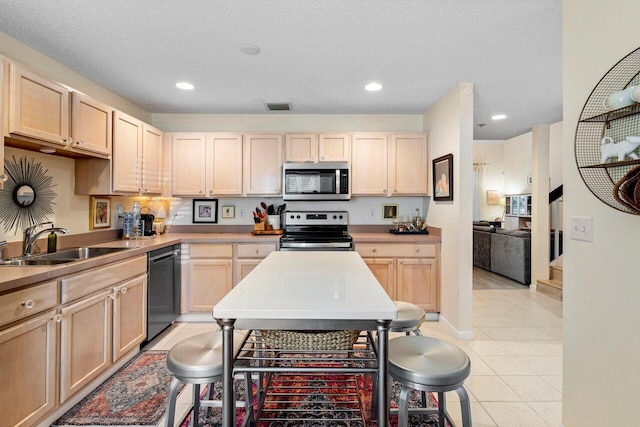 kitchen featuring light brown cabinetry, sink, light tile patterned floors, stainless steel appliances, and a textured ceiling