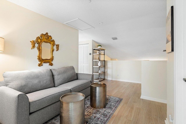 living room with vaulted ceiling, a textured ceiling, and light wood-type flooring