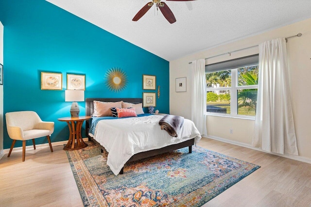 bedroom with ceiling fan, lofted ceiling, a textured ceiling, and light hardwood / wood-style flooring