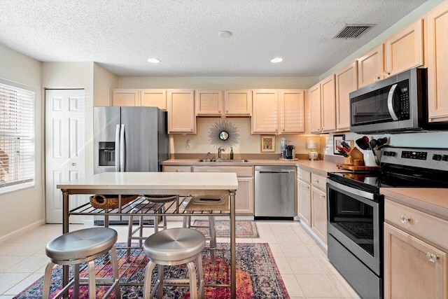 kitchen featuring light tile patterned flooring, light brown cabinetry, sink, stainless steel appliances, and a textured ceiling