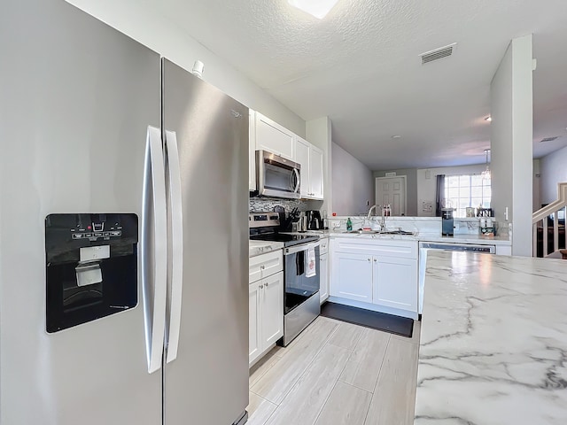 kitchen with sink, kitchen peninsula, stainless steel appliances, light stone countertops, and white cabinets