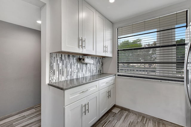 kitchen featuring dark stone countertops, light hardwood / wood-style flooring, decorative backsplash, and white cabinets