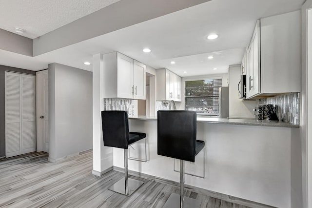 kitchen featuring stainless steel appliances, a breakfast bar, kitchen peninsula, and white cabinets