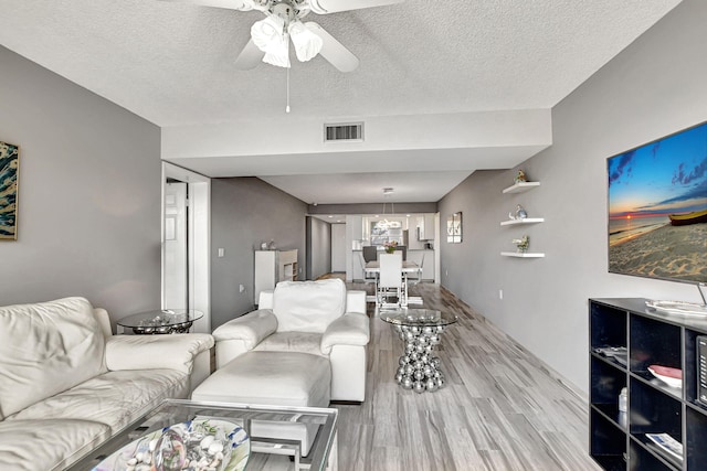 living room with ceiling fan, a textured ceiling, and light wood-type flooring