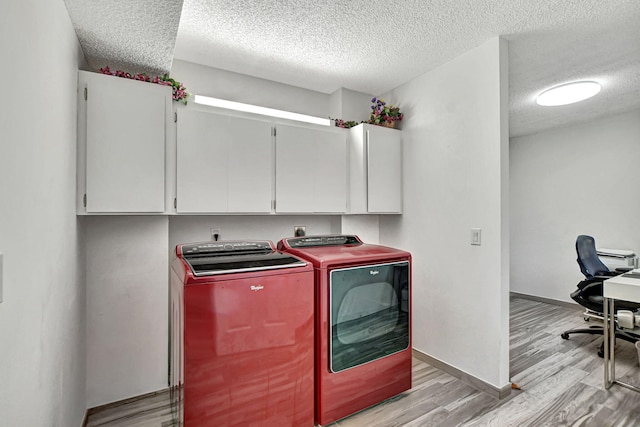 clothes washing area with cabinets, washer and dryer, a textured ceiling, and light wood-type flooring