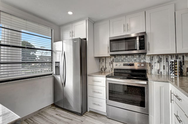 kitchen with white cabinetry, stainless steel appliances, light stone counters, and backsplash