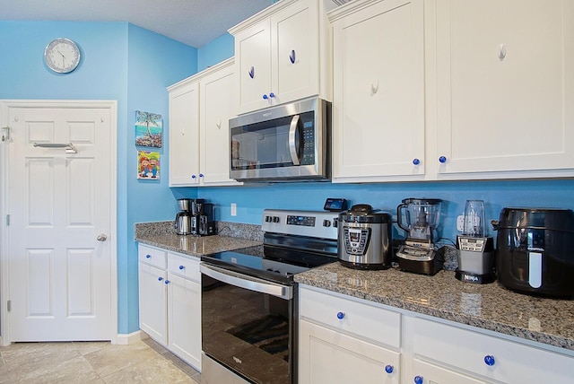 kitchen featuring appliances with stainless steel finishes, dark stone counters, and white cabinetry