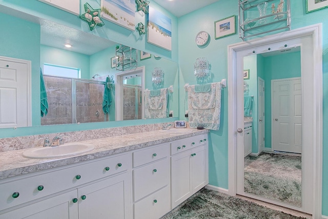 bathroom with a tile shower, double vanity, a sink, and baseboards