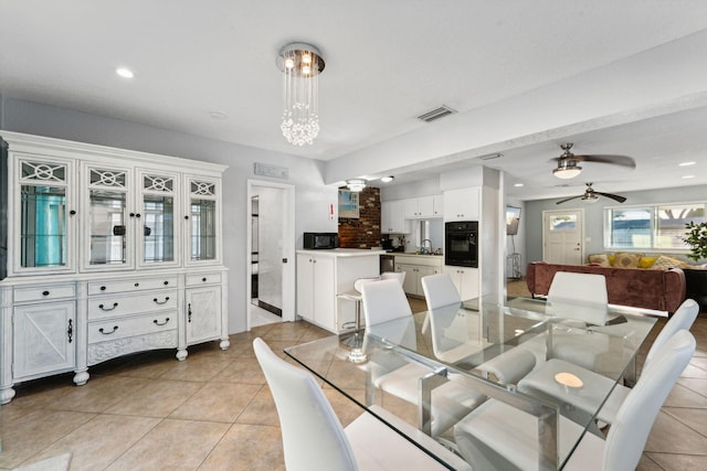 dining area featuring light tile patterned floors, ceiling fan with notable chandelier, and sink