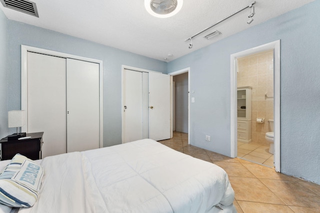 tiled bedroom with rail lighting, multiple closets, and ensuite bathroom